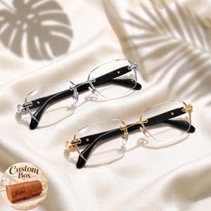 May include: Two pairs of rimless eyeglasses with clear lenses and black temples. One pair features silver-tone metal accents at the hinges and bridge, while the other features gold-tone metal accents. A small circular inset shows a brown leather custom box.