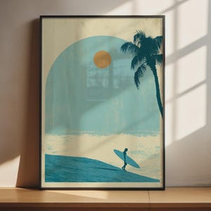 Op de afbeelding: Een ingelijste kunstdruk met een gestileerd strandtafereel met een blauwgroene boog, een gouden zon, een donkerblauwgroene palmboom en het silhouet van een persoon die een surfplank langs de kustlijn draagt, uitgevoerd in een gedempt kleurenpalet.