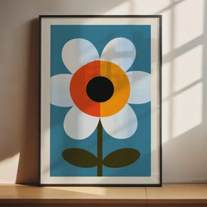Puede incluir: Una lámina enmarcada que muestra una flor estilizada con pétalos blancos, un centro bicolor naranja y amarillo, y un núcleo circular negro. La flor tiene un tallo verde oscuro y dos hojas sobre un fondo de color azul sólido.