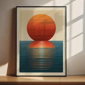 以下が含まれることがあります： 額装された長方形のアートプリント。水平にオレンジと赤のストライプが入った大きな太陽が濃い青色の海の上に描かれています。太陽は水面に明るい線状の反射を作り出し、背景はライトベージュ色です。