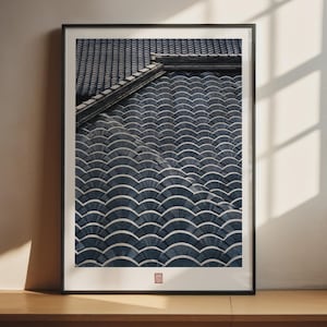 May include: A framed wall art print featuring a high-angle view of dark blue, overlapping semi-circular roof tiles arranged in a repeating pattern. The print includes a small red square seal mark at the bottom centre, encased in a thin black frame.