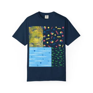 May include: Navy blue t-shirt with a colorful, geometric design. The design is divided into four sections, featuring palm leaves, abstract shapes, anchors, and paper boat patterns. The shirt is made of a soft material.