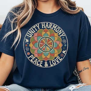 May include: Navy blue t-shirt featuring a colorful circular design with the words "Unity Harmony Peace & Love" surrounding a peace symbol. The design includes floral and star elements in shades of orange, green, and pink.