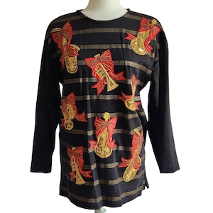 Könnte beinhalten: Schwarzes Langarmshirt mit goldenen horizontalen Streifen. Das Shirt zeigt gestickte Musikinstrumente, darunter Trompeten, Saxophone und Geigen, die jeweils mit einer roten Schleife verziert sind. Die Instrumente sind goldfarben und die Schleifen sind rot.