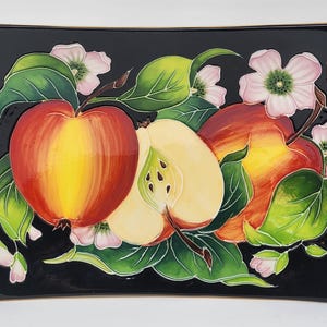 May include: A black ceramic rectangular serving dish with a raised design of three apples and white flowers. The apples are red, yellow, and green. The flowers are white with pink accents.
