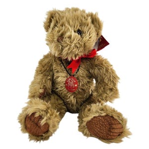 Puede incluir: Un oso de peluche marrón con una cinta roja y un colgante. El oso tiene una textura de pelaje hirsuto y almohadillas marrones. Una etiqueta roja está adherida al oso. El colgante tiene el texto "LIMITED".
