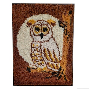 以下が含まれることがあります： 額縁に入った、質感のあるフクロウのタペストリー。フクロウは白、茶色、黄色で描かれ、クリーム色の円と茶色の背景が特徴です。アートワークは濃い茶色の縁で縁取られています。