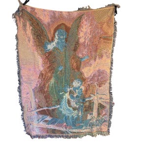 Pu&ograve; includere: Coperta arazzo tessuta raffigurante un angelo e un bambino, nei toni del blu, rosa e marrone. La coperta ha un bordo con frange. L'opera d'arte raffigura una scena religiosa.