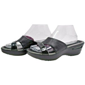 May include: A pair of black leather sandals with a platform sole. The sandals have a glossy strap across the top and a silver trim. The platform sole has a slight wedge and a visible air pocket. The sandals are displayed on clear plastic forms.