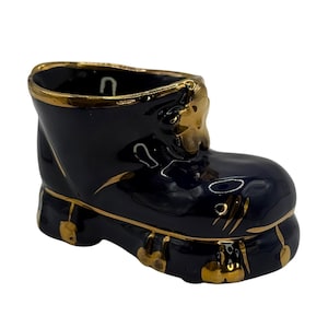 Könnte beinhalten: Ein kleiner, keramikartiger Stiefel-Dekorationsartikel. Der Stiefel ist marineblau mit goldenen Akzenten an den Rändern und dekorativen Elementen. Er hat eine glänzende Oberfläche und einen hohlen Innenraum.