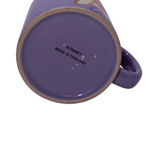 Puede incluir: Una taza de cer&aacute;mica morada con asa. La base de la taza tiene el texto "&copy; DISNEY MADE IN THAILAND". La taza es de color morado liso.