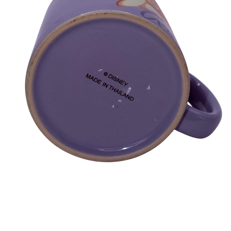 Puede incluir: Una taza de cer&aacute;mica morada con asa. La base de la taza tiene el texto "&copy; DISNEY MADE IN THAILAND". La taza es de color morado liso.