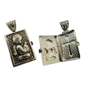 Puede incluir: Colgante rectangular plateado con una imagen en relieve de un querubín. El colgante se abre para revelar un ángel y una cruz. Tiene una fianza decorativa para una cadena. El colgante se muestra abierto y cerrado.