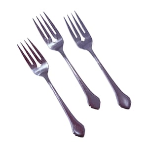 May include: Three silver forks with a decorative diamond-shaped cutout in the tines. The forks have long, slender handles with a rounded, ornate design at the base. The forks are arranged diagonally against a white background.