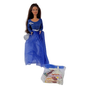 May include: A doll wearing a long blue dress with a silver belt and a matching purse. The doll has long brown hair and is holding a small silver purse. A package of toy food and accessories is at the doll's feet.