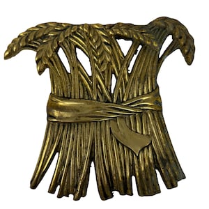 Pode incluir: Um ornamento de metal dourado em forma de espiga de trigo. A espiga é amarrada com uma fita e tem um desenho em forma de coração na parte inferior.
