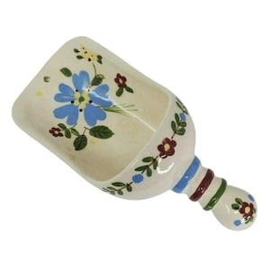 Puede incluir: Cucharón de cerámica color crema con diseño floral. El cucharón presenta una flor azul con hojas verdes y detalles rojos y amarillos. El mango está decorado con rayas azules, burdeos y verdes y un pequeño diseño floral.