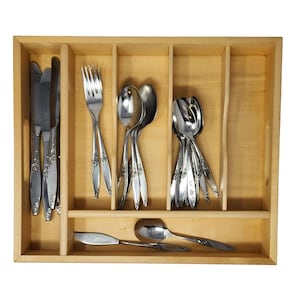 May include: A wooden cutlery organizer filled with stainless steel silverware. The set includes knives, forks, and spoons, each with a decorative floral pattern on the handles. The organizer is divided into compartments for easy storage.