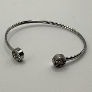 May include: A silver bangle bracelet with two round, clear crystal-encrusted accents.