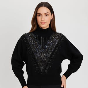 May include: A black turtleneck jumper featuring a V-shaped beaded pattern across the chest. The design uses geometric shapes and a mix of dark and iridescent beads. The jumper has long sleeves and a ribbed collar.