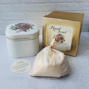 May include: A white ceramic jar with a floral design on the lid, a gold-colored box with the words "Royal Secret", and a bag of powder. The jar has a gold band around the middle. The box has a floral design and the words "Royal Secret".