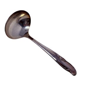 May include: A shiny, silver-colored ladle with a rounded bowl and a long, slender handle. The handle features a decorative floral design near the end. The ladle is designed for serving soups, sauces, or other liquids.