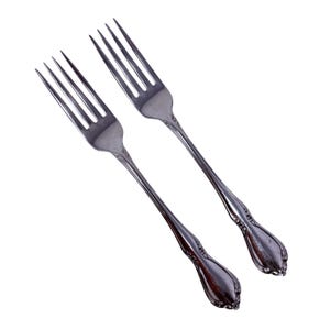 May include: Two silver forks with four tines each, angled against a white background. The handles have a decorative, ornate design. The forks are likely for a formal dining setting.