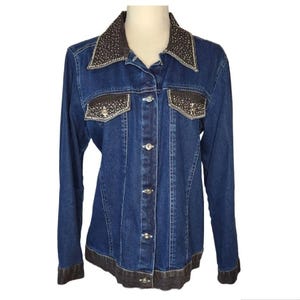 May include: A dark blue denim jacket with long sleeves, a button-up front, and a dark brown collar and pocket accents. The collar and pockets are embellished with small, sparkling rhinestones. The jacket has a dark brown hem.