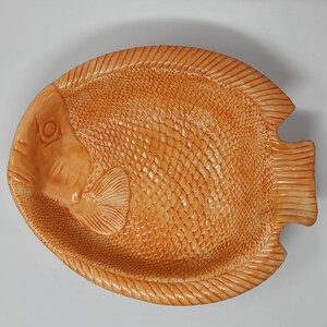 May include: A ceramic serving dish shaped like a fish. The dish is a light orange colour and has a detailed design of scales.