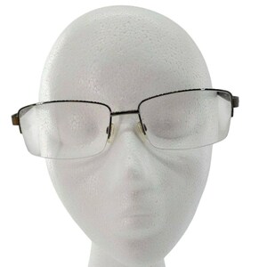 May include: Rectangular eyeglasses with a dark metal frame and clear lenses. The glasses have a half-rim design, with the frame extending across the top and sides of the lenses. The nose pads are a light color. The glasses are displayed on a white foam head.