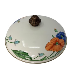 May include: A white ceramic lid with a bronze knob. The lid features orange and blue poppy flowers, green leaves, and turquoise buds. The rim is trimmed with a gold-coloured band.