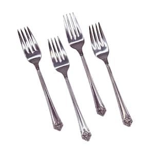 Op de afbeelding: Vier zilveren vorken met tanden en decoratieve handvatten zijn diagonaal geplaatst tegen een witte achtergrond. De vorken hebben een klassiek ontwerp, geschikt voor formele diners. De handvatten hebben een sierlijk, reliëfpatroon.