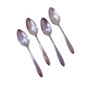 May include: Four vintage silver spoons arranged diagonally on a white background. The spoons have oval bowls and long, slender handles. The spoons show signs of wear, with some tarnishing visible on the silver surface. The spoons are likely for serving or eating.