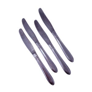 May include: Four stainless steel dinner knives with a decorative pattern on the handles. The knives are arranged diagonally against a white background, showcasing their polished blades and elegant design. Ideal for formal dining settings.