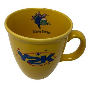 May include: Yellow ceramic mug with a curved handle. The mug features the text "Y2K" in blue, along with a cartoon bug and the phrase "Gonna Getcha!" in black. The mug has a glossy finish.