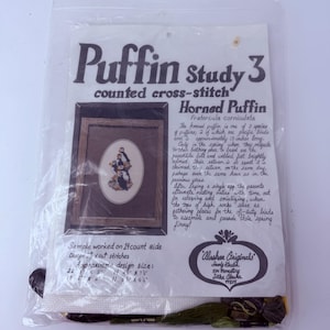 May include: A cross-stitch kit featuring a framed image of Horned Puffins. The kit includes the text "Puffin Study 3" and "Alaskan Originals." The design size is approximately 5 x 7.75 inches.