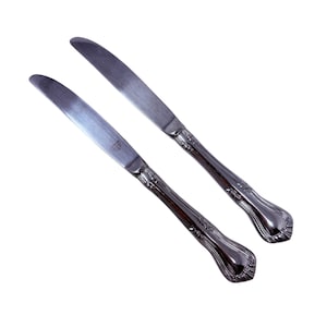以下が含まれることがあります： 装飾的で湾曲したハンドルが付いた、ステンレス鋼製のバターナイフ2本。 刃は滑らかで反射性があり、ハンドルには詳細な花の模様があります。 ナイフはわずかに角度がつけられており、エレガントな形状を示しています。