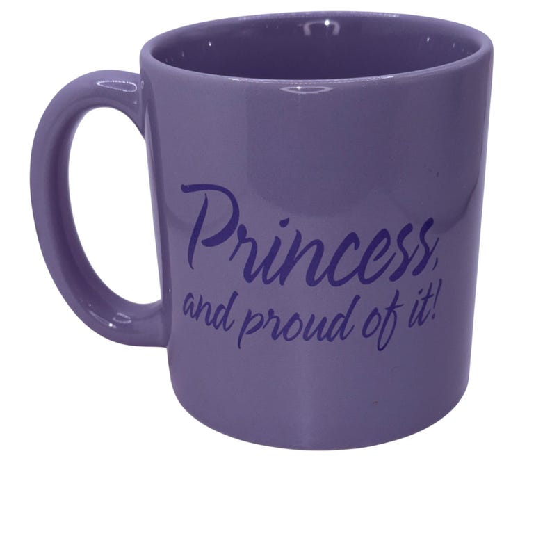 Puede incluir: Una taza de cer&aacute;mica lavanda con un asa curvada. La taza presenta el texto "Princess, and proud of it!" en una fuente de escritura. La taza es de color s&oacute;lido y tiene un acabado brillante. Ideal para caf&eacute;, t&eacute; o cualquier bebida.