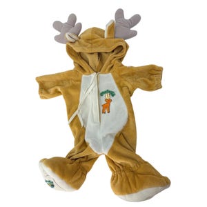 May include: A tan and white plush reindeer costume with a hood and attached antlers. The costume features a white front panel with a deer applique and a zipper closure. The feet have white accents and a small embroidered design.