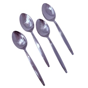 Può includere: Quattro cucchiai in acciaio inossidabile disposti diagonalmente su sfondo bianco. Ogni cucchiaio ha una coppa arrotondata e un lungo manico con un motivo floreale all'estremità. I cucchiai sono riflettenti, mostrando l'ambiente.