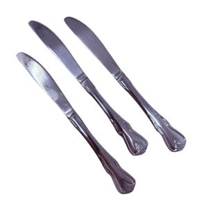 May include: Three stainless steel butter knives with a decorative floral pattern on the handles. The blades are smooth and slightly curved. The knives are arranged diagonally against a white background.