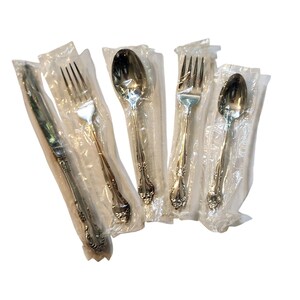 Puede incluir: Un juego de cinco cubiertos, que incluye un cuchillo, tenedores y cucharas, envueltos individualmente en plástico transparente. La cubertería tiene un diseño floral decorativo en los mangos.