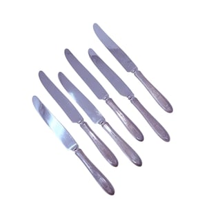Peut inclure: Six couteaux argentés disposés en diagonale sur fond blanc. Chaque couteau a une longue lame fine et un manche décoratif. Les couteaux sont probablement destinés à un cadre de restauration formel.