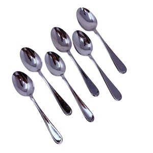 Puede incluir: Un juego de siete cucharas brillantes de acero inoxidable dispuestas en diagonal sobre un fondo blanco. Cada cuchara tiene un cuenco redondeado y un mango delgado. Las cucharas reflejan la luz, creando una apariencia brillante y limpia. Ideal para servir o comer.