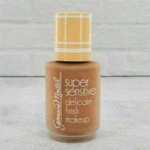 Op de afbeelding: Een klein flesje Germaine Monteil Super Sensitive Delicate Finish Makeup. De fles is bruin met een gouden dop en witte letters.