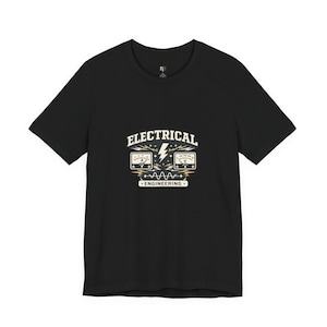 May include: Black t-shirt with a white and beige graphic. The graphic features the words "ELECTRICAL ENGINEERING" above two meter displays and a lightning bolt. The shirt is a crew neck style.
