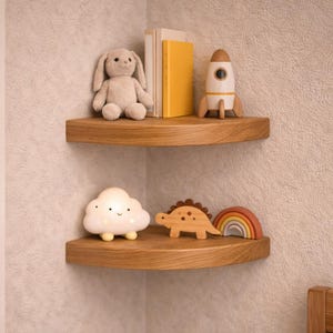 Op de afbeelding: Twee houten hoekplanken tonen kinderspeelgoed. De bovenste plank bevat een knuffelkonijn, boeken en een raket. De onderste plank heeft een wolk-vormig nachtlampje, een houten dinosaurus en een regenboog.