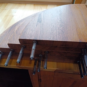 K&ouml;nnte beinhalten: Ein Stapel aus vier dreieckigen Holzregalen mit einer nat&uuml;rlichen braunen Holzmaserung. Jedes Regal verf&uuml;gt &uuml;ber vorinstallierte graue Kunststoff-Wandd&uuml;bel, die an der Unterseite hervorstehen und zur Wandmontage der Regale dienen.