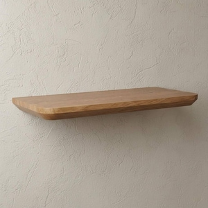 May include: A rectangular floating wall shelf made of light brown wood with a smooth, polished surface and beveled edges. The shelf features a natural wood grain pattern and is mounted horizontally, providing a flat, stable surface for display.