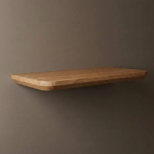 Pode incluir: Uma prateleira flutuante de madeira retangular com grão de madeira natural. A prateleira tem bordas arredondadas e é montada em uma parede de cor neutra. A prateleira tem aproximadamente 76 cm de comprimento.